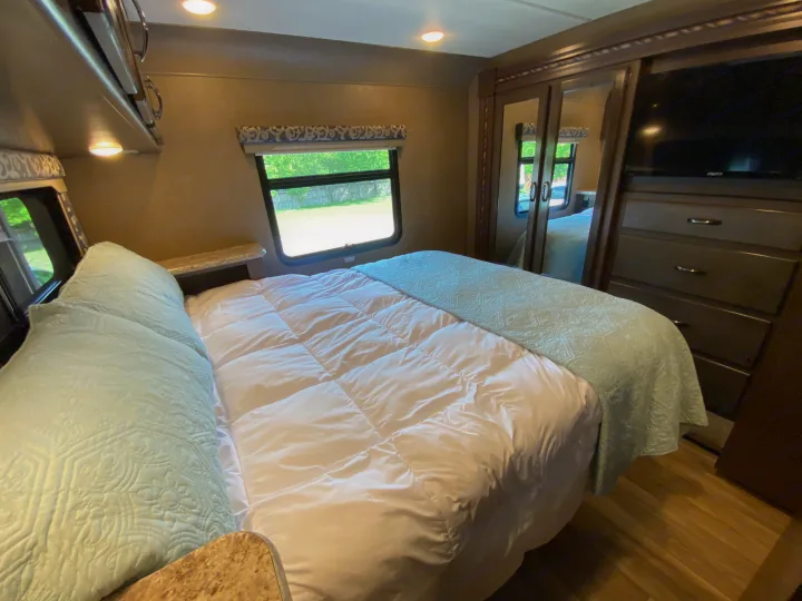 RV rental bedroom: cozy space with bed, storage, TV, window. Light blue & white decor, wood-look floor.. Thor Motor Coach Four Winds with full wall slide 2018