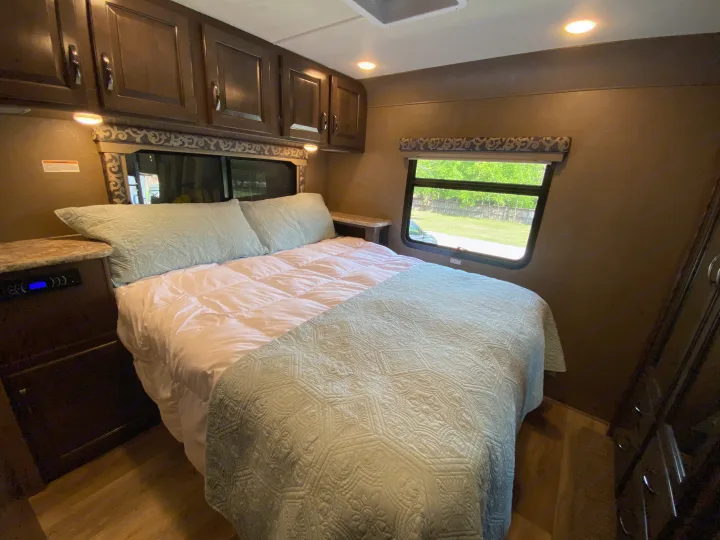 Bright RV rental bedroom featuring a comfy bed with blue quilt, wood cabinets, and a window overlooking nature.. Thor Motor Coach Four Winds with full wall slide 2018