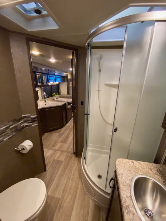 RV rental: Modern interior featuring a full bathroom with toilet, sink, and curved shower, plus a view into the living space.. Thor Motor Coach Four Winds with full wall slide 2018
