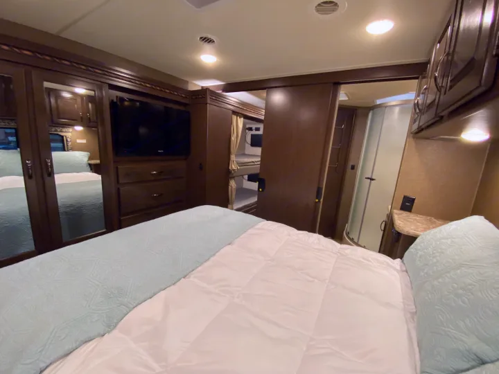 Explore this RV rental's bedroom: comfy bed, mirrored closet, TV, built-in bunks, and private shower area.. Thor Motor Coach Four Winds with full wall slide 2018