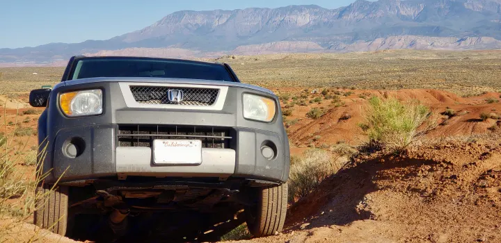 A Honda Element off-road in a red desert landscape with mountains. A distant RV rental suggests extended outdoor adventure.. Honda Element 2003