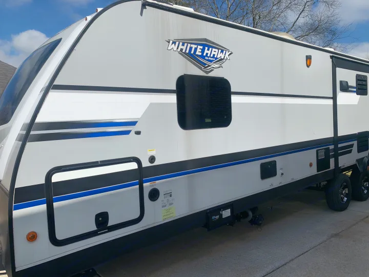 A White Hawk travel trailer, white and grey with blue accents, parked. Ideal for an RV rental getaway.. Jayco White Hawk 2018