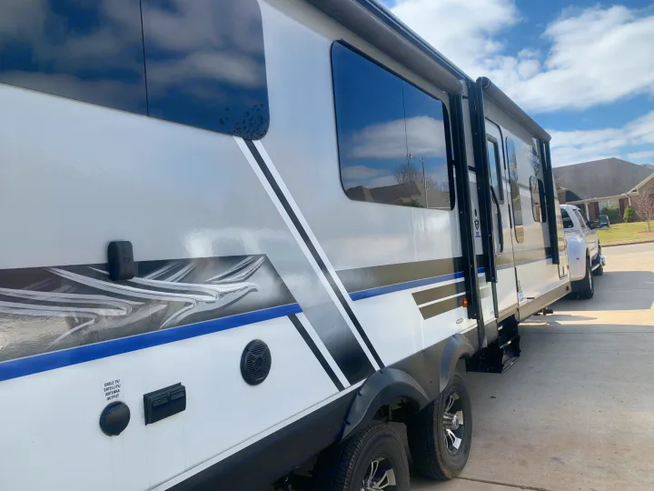 Side view of a modern white and grey travel trailer, ready for an RV rental adventure. Parked on a driveway with a truck.. Jayco White Hawk 2018