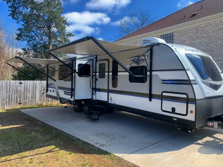 Spacious RV rental travel trailer with dual extended awnings, set up for outdoor living on a concrete patio.. Jayco White Hawk 2018