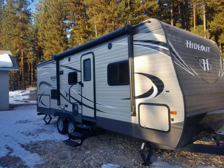 This photo shows the door, stairs, awning rolled up, storage compartment (front), and compartment where outdoor kitchen is (rear). . Keystone Hideout 2017