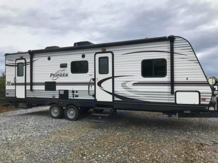 This white & gray Pioneer travel trailer, ideal for rv rental, features multiple windows, two doors, and an awning for your journey.. Heartland Pioneer 2016