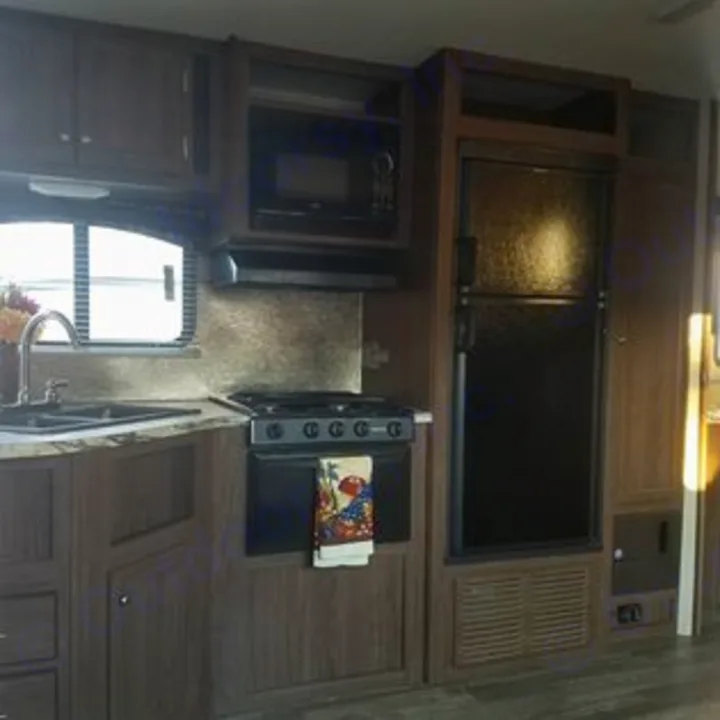 Compact RV rental kitchen features dark wood cabinets, microwave, stovetop, sink, & black fridge. Perfect for your road trip.. Heartland Pioneer 2016