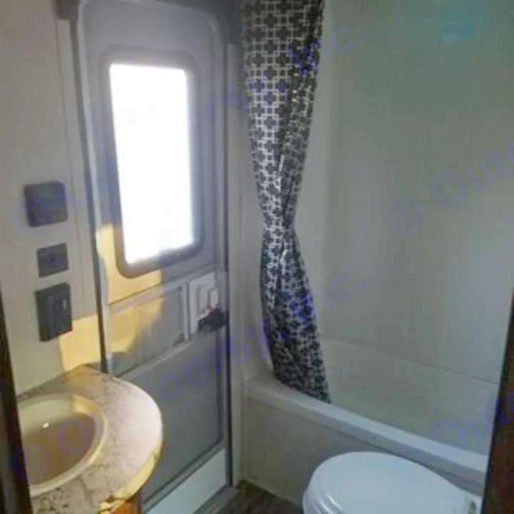 This RV rental bathroom features a compact sink, bright door, shower with patterned curtain, and toilet.. Heartland Pioneer 2016
