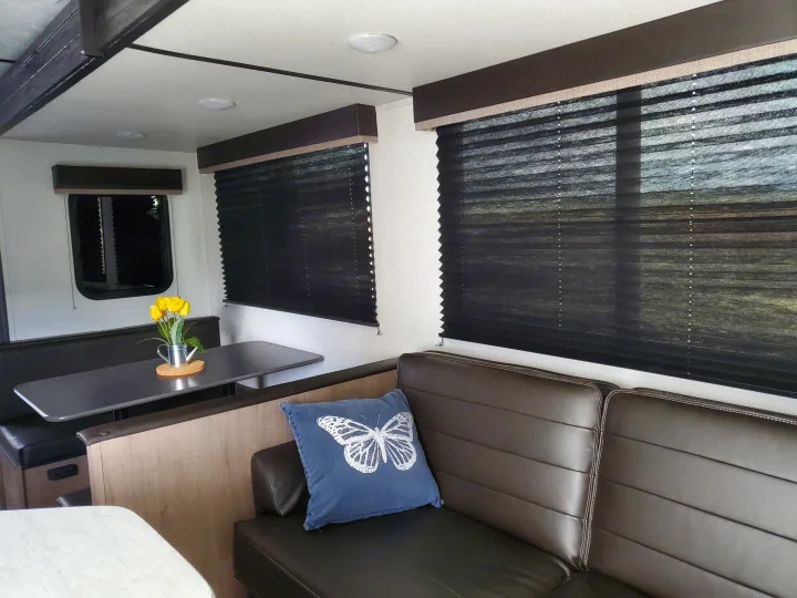 Comfortable rv rental interior featuring a dining booth, brown sofa with a butterfly pillow, and yellow flowers on the table.. Keystone RV Hideout 2021