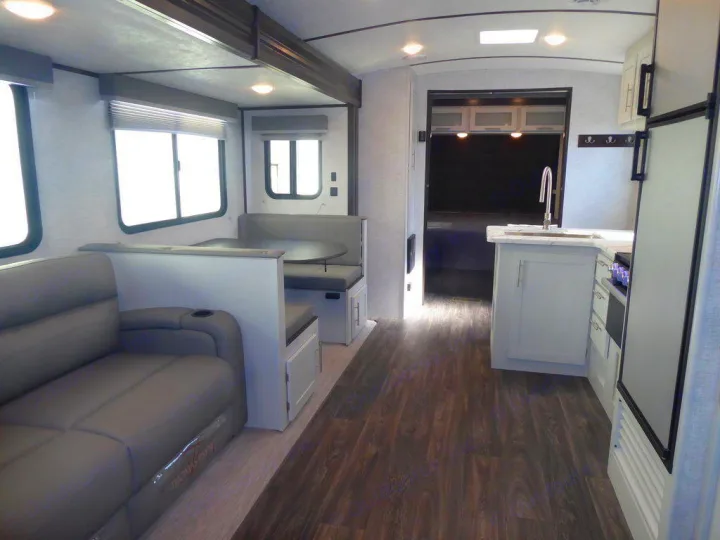 Interior of a modern RV rental, showing a gray couch, dinette, and kitchen with light cabinetry and wood flooring.. Keystone Bullet 2021