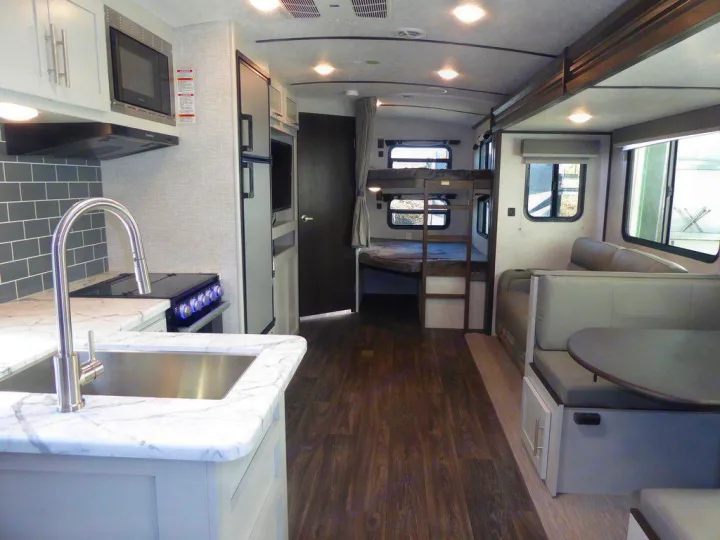 Interior of an RV rental: kitchen on left, dinette and bunk beds on right. Comfortably designed for travel.. Keystone Bullet 2021