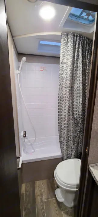 RV rental bathroom showing a compact shower/tub combo, toilet, bright ceiling light, and vent/skylight.. Jayco Jay Flight 2021