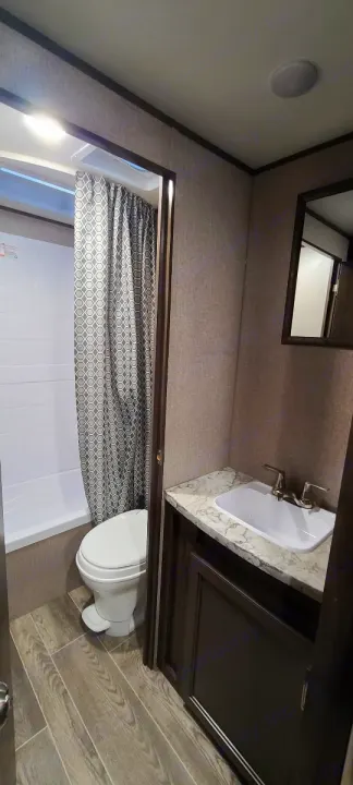 Inside a modern RV rental bathroom. Features include a shower/tub, toilet, and sink vanity with mirror for comfortable travel.. Jayco Jay Flight 2021