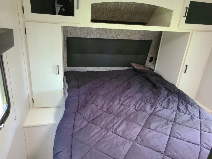 This cozy RV rental bedroom features a dark comforter, upholstered headboard, and light cabinetry, offering comfortable travel lodging.. Venture Rv 261 VBH 2021