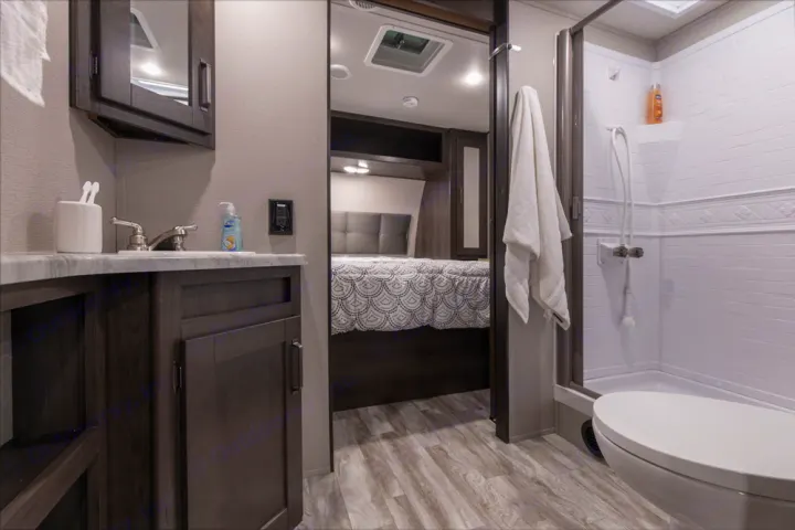 Modern RV rental interior showcasing a compact bathroom with sink, shower, toilet, and an adjacent cozy bedroom.. Grand Design Other 2022