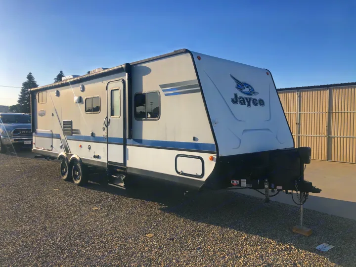 A white Jayco travel trailer RV rental with blue stripes, parked on a gravel lot under a clear sky.. Jayco Jay Feather 2018
