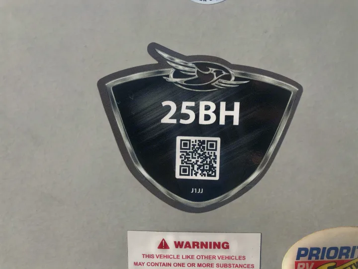 Close-up of an RV rental model '25BH' badge featuring a QR code and a partial vehicle warning label.. Jayco Jay Feather 2018