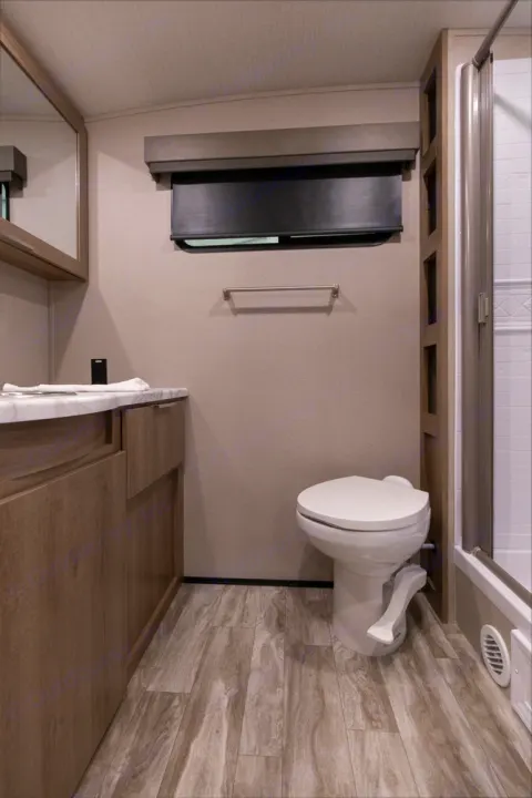 Inside a modern RV rental, this compact bathroom features a toilet, vanity with sink, and glass-enclosed shower.. Grand Design Other 2021