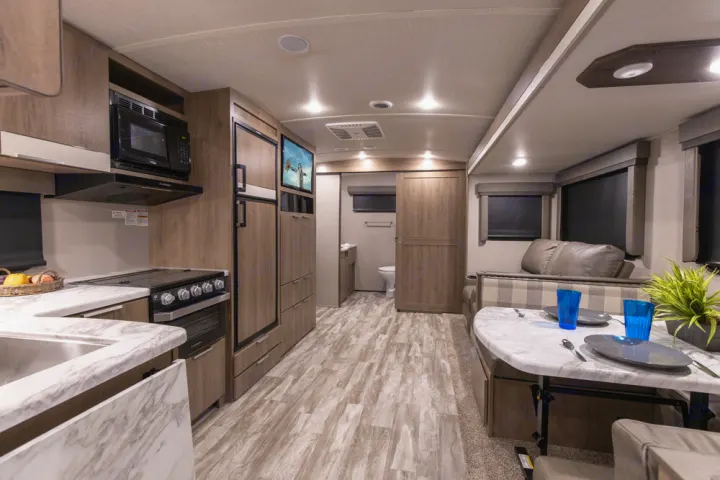 Modern RV rental interior: fully equipped kitchen, dining area with booth, and rear bathroom visible through an open door.. Grand Design Other 2021