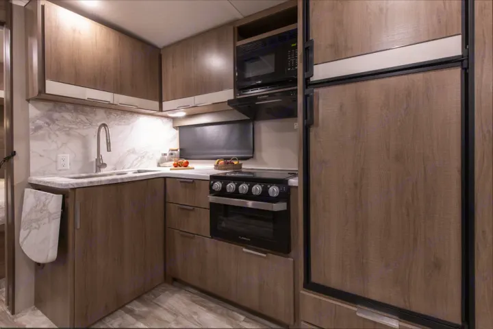 Modern RV rental kitchen showcasing compact design: wood cabinets, marble counters, and essential appliances.. Grand Design Other 2021