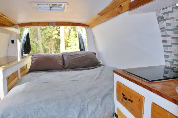 Cozy rv rental interior: A comfy bed, compact kitchen, and forest views for your next camping or road trip adventure.. Ford Econoline 2009