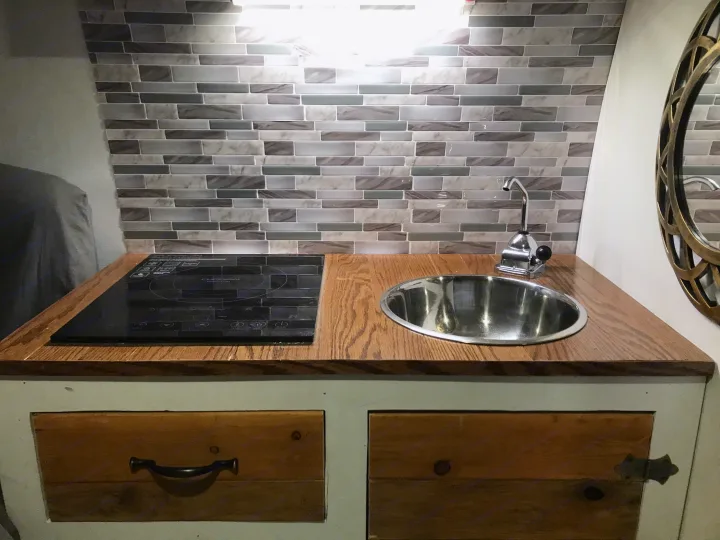 Compact RV rental kitchen featuring a wood countertop, built-in induction cooktop, stainless steel sink, and stylish tiled backsplash.. Ford Econoline 2009