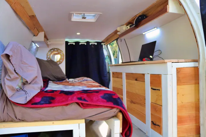 RV rental: Cozy camper van interior featuring a bed, wooden workspace with a laptop, and functional storage.. Ford Econoline 2009