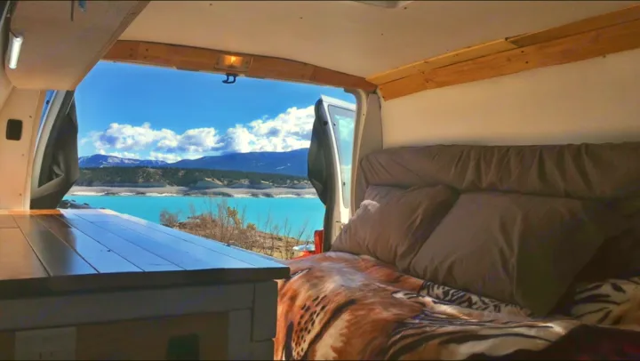 This RV rental offers a cozy bed & stunning views! Perfect for van life, with a turquoise lake, mountains, and blue sky just outside.. Ford Econoline 2009