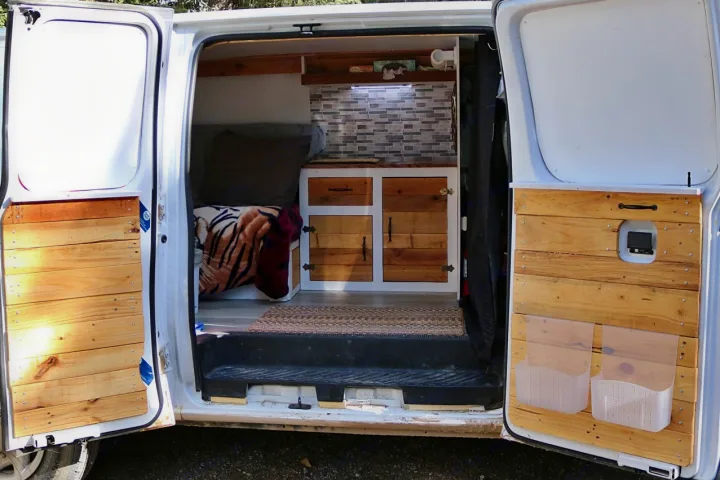Explore this charming RV rental interior with a custom wood bed, kitchenette, and door storage in a camper van.. Ford Econoline 2009