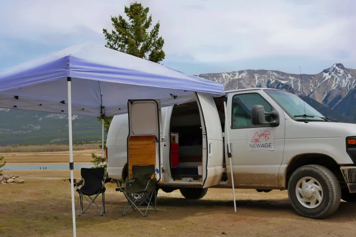 White RV rental camper van with open doors under a canopy, chairs, mountains & lake. Ideal for a getaway.. Ford Econoline 2009