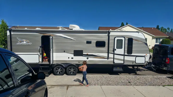 An RV rental, a Jayco travel trailer, hooked up in a sunny driveway with kids loading for a family trip.. Jayco Jay Flight 2020