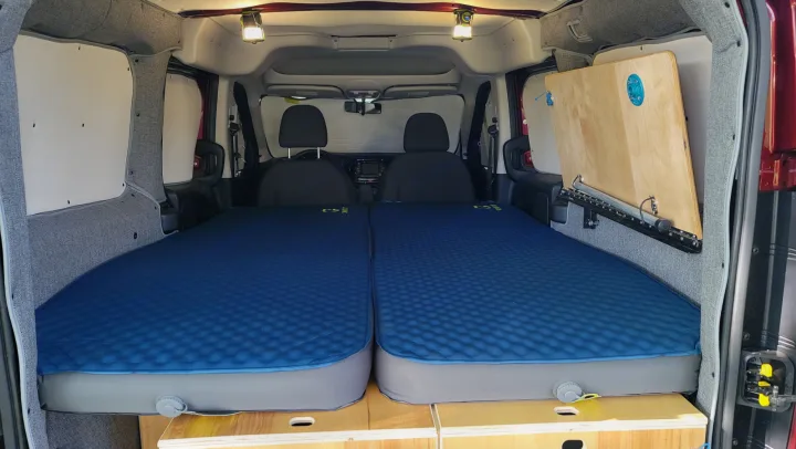 Cozy rv rental camper van interior: twin sleeping mats on wooden storage, side panels, overhead lights, and a folding table.. RAM Promaster CIty 2018