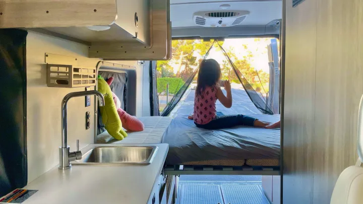 Spacious RV rental camper van: child on bed enjoying the view, with kitchen area.. Winnebago Solis 2022