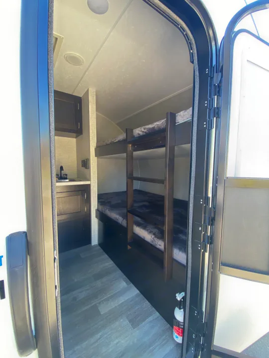 This RV rental interior offers space-saving bunk beds, a compact sink area, and a fire extinguisher for safety.. Bushwacker 17BH 2021