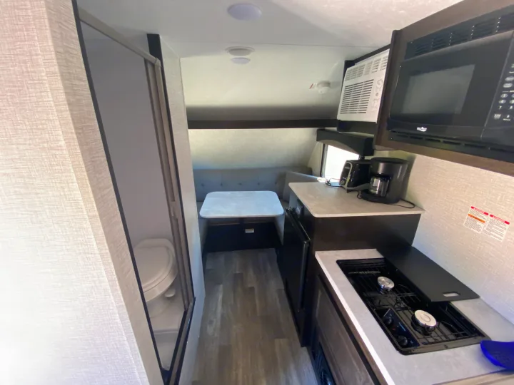This RV rental offers a compact interior featuring a full kitchen with stove and microwave, a cozy dinette, and a small bathroom, ideal for travel.. Bushwacker 17BH 2021