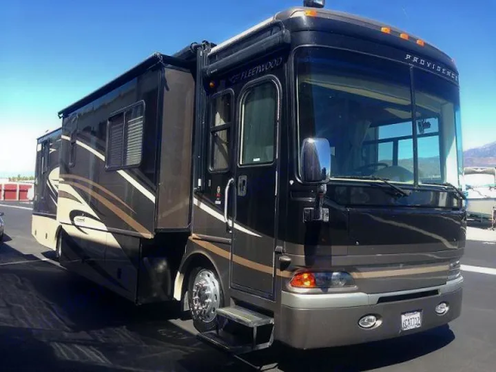 Large, dark Fleetwood Providence motorhome for rv rental, featuring striped design, parked outdoors on a sunny day.. Fleetwood Providence 2010