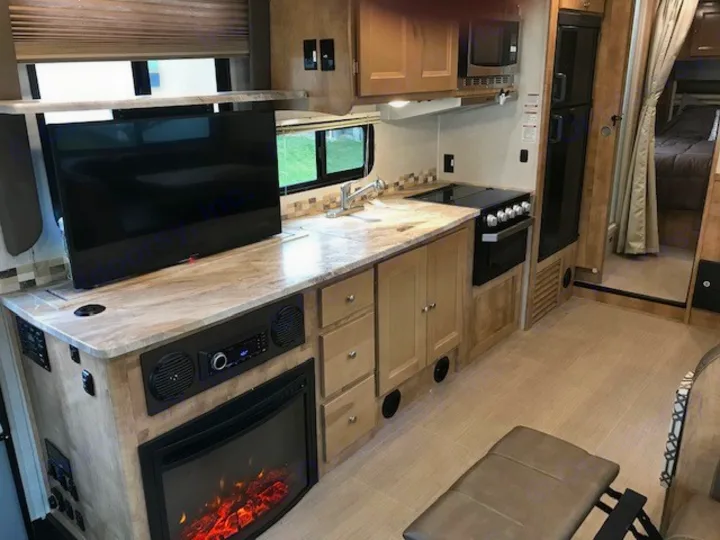 Spacious RV rental interior with a fully equipped kitchen, living area with TV/fireplace, and cozy bedroom beyond.. Coachmen Leprechaun 2018
