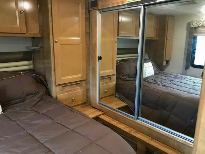 Cozy RV rental bedroom with two comfortable beds, wood cabinets, and mirrored sliding wardrobe for storage.. Coachmen Leprechaun 2018