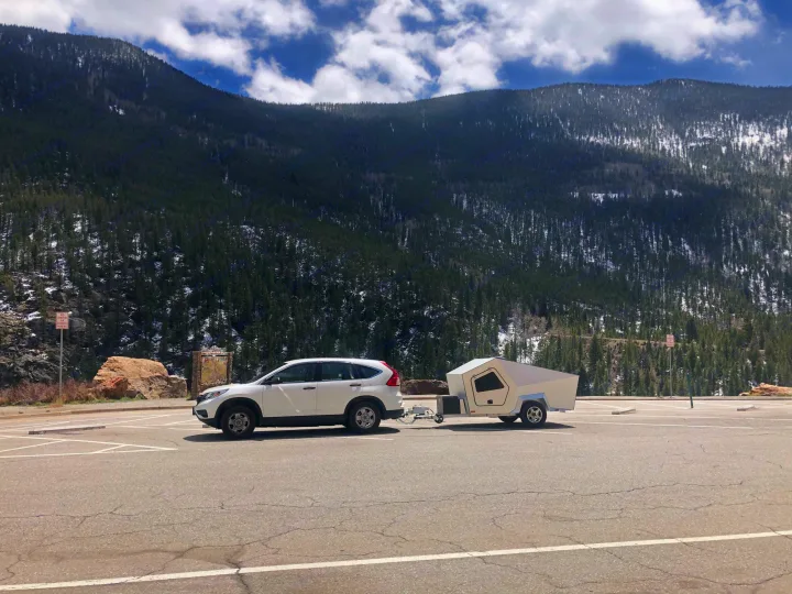 White SUV towing a small, modern camper trailer in a scenic mountain parking lot, ideal for an RV rental trip.. Polydrop K-20 2020