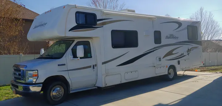 This white Sunseeker Class C RV rental, a Ford E-450 recreational vehicle, is parked on a sunny driveway, ready for adventure.. Forest River Sunseeker 2012
