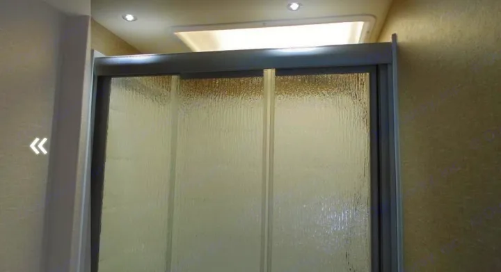 RV rental bathroom's compact shower with textured glass sliding doors, brightened by an overhead skylight.. Dynamax Corp Isata 2016