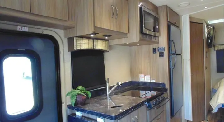 RV rental interior: A functional kitchen with microwave, fridge, and sink, plus an exit door for adventures.. Dynamax Corp Isata 2016