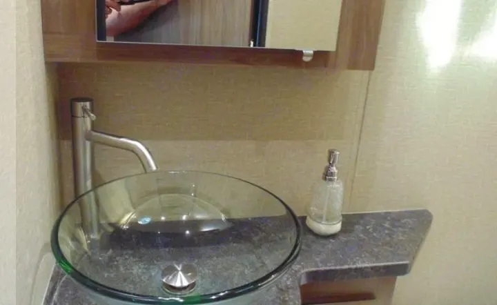 A compact RV rental bathroom showcases a chic glass vessel sink, modern faucet, and soap dispenser on a dark vanity.. Dynamax Corp Isata 2016