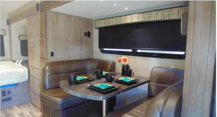 Cozy RV rental interior with a dining booth, table set with dishes & mugs, and adjacent bedroom. Perfect for your travels!. Dynamax Corp Isata 2016