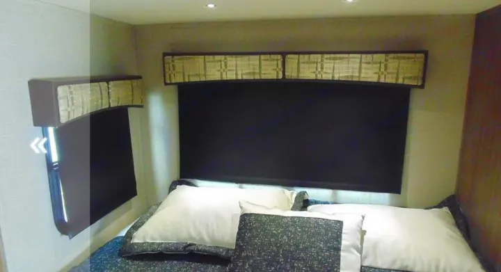 Step into this comfortable RV rental bedroom, featuring a plush bed, dark window shades, and stylish valances.. Dynamax Corp Isata 2016