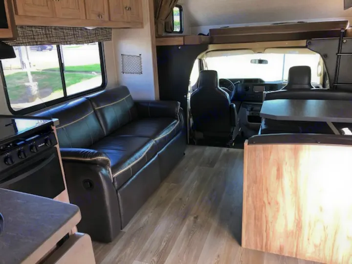 View of a modern RV rental interior showing a brown leather sofa, kitchen, wood floor, and front cockpit area.. Forest River Other 2017