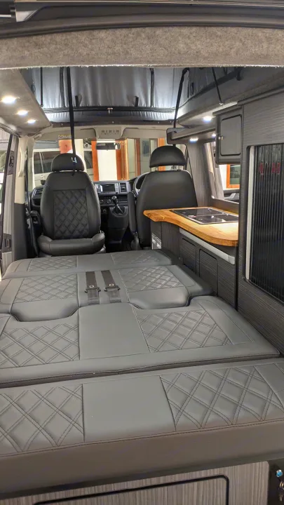 Modern RV rental interior: custom diamond-stitched seating, wooden kitchen counter, and LED lighting.. vw T6 2016