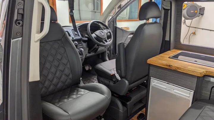 RV rental interior: Quilted black seats, driver's cockpit, and compact kitchenette with sink and fridge.. vw T6 2016