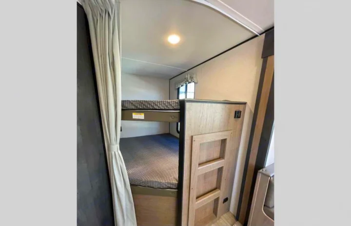 Step inside this RV rental's cozy interior, featuring comfortable bunk beds with patterned mattresses, a privacy curtain, and a window.. Other Hideout 2021