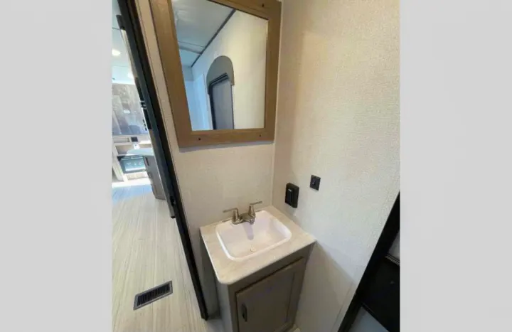 RV rental: Clean, compact bathroom featuring a modern sink, wooden vanity, and wall mirror. Reflects light-toned RV interior.. Other Hideout 2021